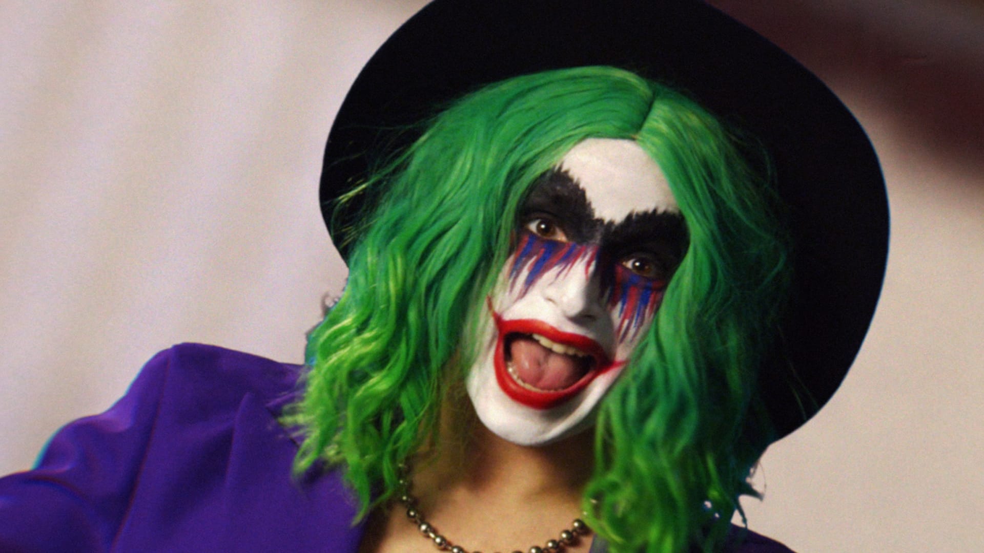 woman with green hair and joker clown make up smiling wide while staring at the camera