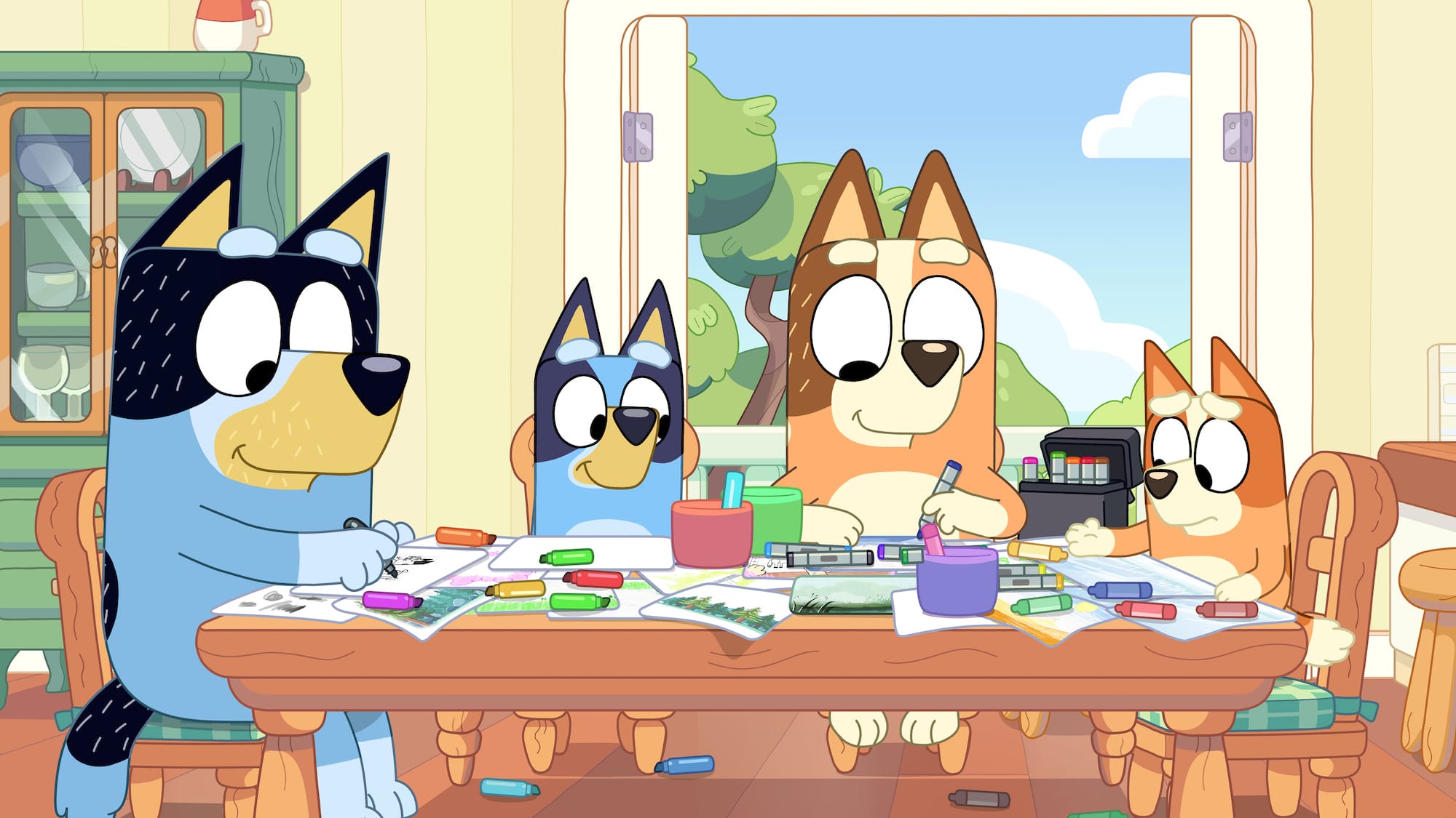 Bandit, Bluey, Chili, and Bingo drawing together at their kitchen table, which is covered in art supplies